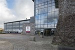 A tall glass fronted building with an open courtyard and a car park in front