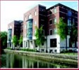 A four storey red brick building on the bank of a canal.